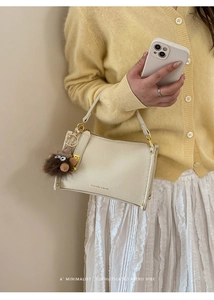 Detail of cream lychee leather handbag with gold hardware and brown plush monster charm