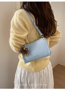 Model view of light blue leather square shoulder bag with cute plush monster charm detail