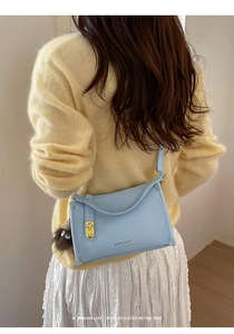 Close-up of light blue pebble leather crossbody bag with fluffy charm and gold hardware