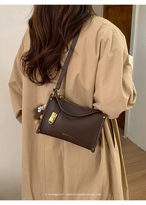 Detail of a dark brown pebble leather crossbody bag with a cute plush charm and gold hardware