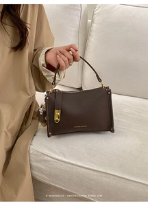 Close-up of deep brown lychee texture leather handbag with gold buckle and plush charm