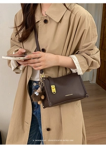 Detail of dark brown lychee leather crossbody bag with gold buckle and plush charm