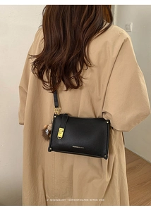 Detail of black lychee leather crossbody bag with gold hardware and cartoon plush charm