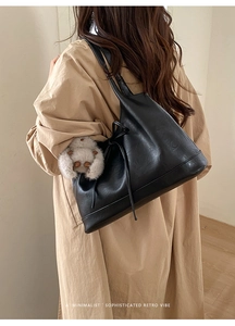Minimalist black leather shoulder bag with plush bear charm worn over a beige trench coat