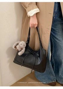 Minimalist black tote bag with a decorative bow and plush rabbit charm detail