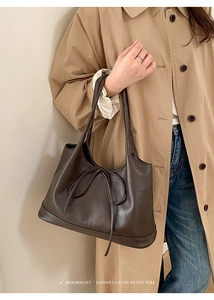 Close-up of a dark brown leather tote bag with elegant bow detail on a classic trench coat