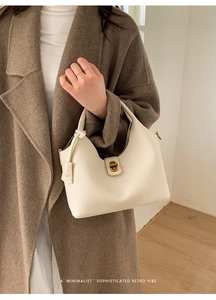 Detailansicht der cremefarbenen Lederhandtasche mit Goldverschluss auf Wollmantel