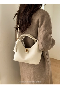 Close-up of cream leather bucket bag with gold twist lock on dark wool coat
