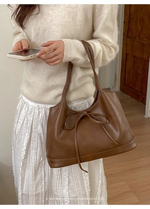 Detail shot of a brown leather shoulder bag featuring a minimalist retro bow knot design