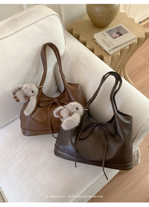 Detail of caramel and dark brown PU leather tote bags with cute bunny charms on a white sofa