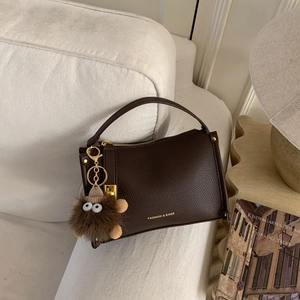 Dark brown pebble leather handbag with gold hardware and plush charm on a white sofa