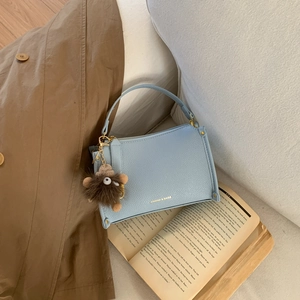 Light blue faux leather handbag with plush charm and chain strap on a cozy background