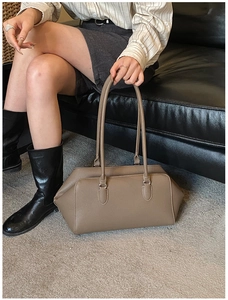 Detail of dark khaki pebbled leather bowling bag on a grey rug with minimalist vibe