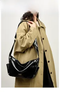 Side view of a glossy black patent leather tote bag styled with a classic beige trench coat