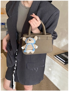Detail of olive green tote bag with silver metal buckles and a cute bear bag charm accessory
