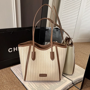 Close-up of woven tote bag showing beige texture, brown leather trim, and metal brand logo
