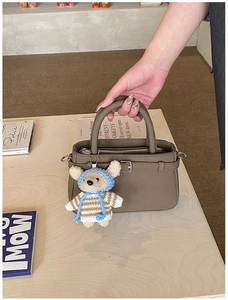 Detail of taupe tote bag with buckle strap and cute teddy bear charm on wood surface