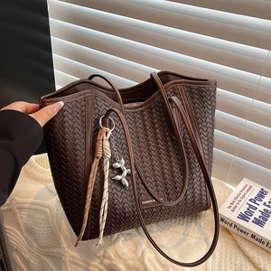 Close-up of dark brown woven leather tote with decorative silver dog charm and shoulder strap