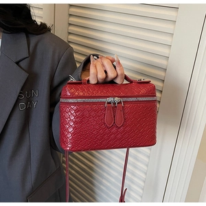 Detalle de bolso rojo con diseño trenzado, cremallera plateada y asa superior