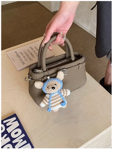 Detail view of khaki leather tote bag featuring a cute knitted bear plush charm
