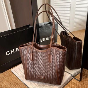 Detailed view of dark brown woven tote bag with silver logo plaque on a magazine
