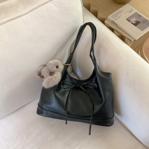 Minimalist black faux leather underarm bag with bow detail and plush charm on a sofa
