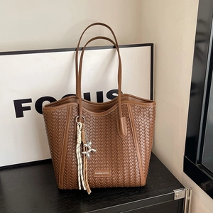 Detail of brown woven tote bag featuring a decorative silver dog charm and tassels