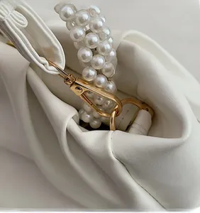 Close-up of golden metal buckle and pearl woven strap on white pleated leather bag