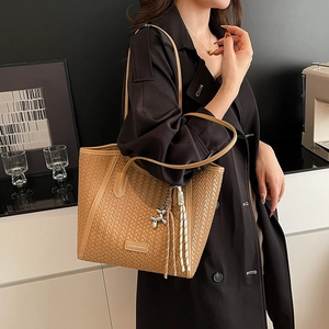 Detail of a brown woven tote bag with silver balloon dog pendant and textured tassel