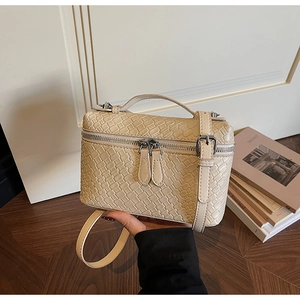Detalle de textura tejida crema y cremalleras plateadas en bolso bandolera elegante