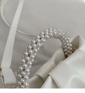 Detail of white pleated handbag featuring elegant faux pearl handle and gold metal hardware