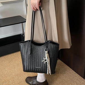Detail of black woven tote bag featuring silver balloon dog charm and tassels