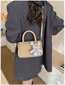 Rear view of model in grey blazer holding a beige lychee leather tote bag with bear charm