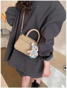 Detail view of khaki leather tote bag with a cute teddy bear charm on grey blazer outfit