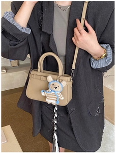 Detail of khaki leather mini tote bag featuring a cute teddy bear charm on adjustable strap