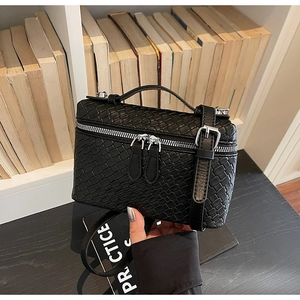 Detalle del bolso de mano negro trenzado con cremallera plateada y correa ajustable