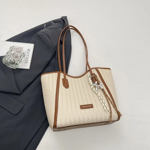 Detail of woven tote bag featuring beige texture, brown leather trim and silver charm