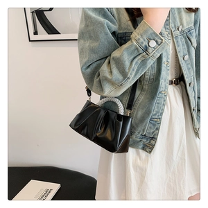 Detail of black pleated cloud handbag featuring white pearl handle and leather shoulder strap