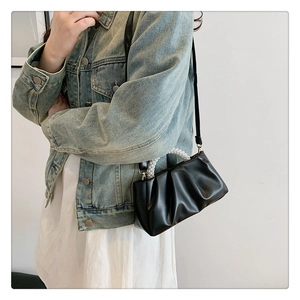 Close-up of black pleated handbag with elegant pearl handle and thin shoulder strap