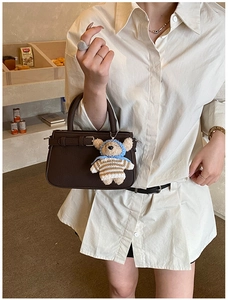 Macro shot of dark brown lychee grain leather tote bag with cute plush bear charm accessory