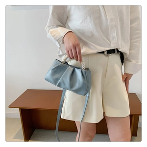 Close-up of light blue pleated cloud bag with elegant pearl handle and PU leather strap