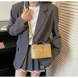 Detalle de bolso bandolera de cuero trenzado dorado con asa y textura metálica