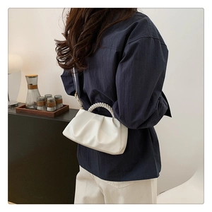 Detail of white pleated cloud bag with elegant pearl handle and adjustable shoulder strap