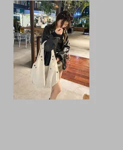 Détail d'un sac Hobo en toile beige avec clous argentés dans un décor extérieur ensoleillé