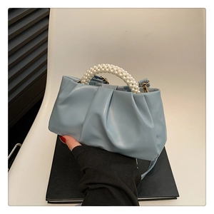 Detail of light blue pleated cloud bag featuring elegant white pearl bead handle