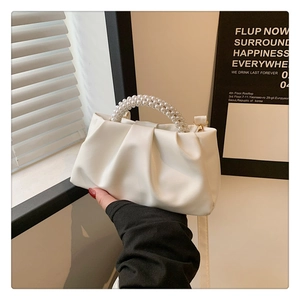 Detail of white pleated cloud bag featuring double-row pearl handle and soft leather texture
