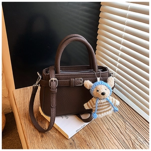 Detail of vintage brown leather tote bag with cute plush bear charm on a wooden stand