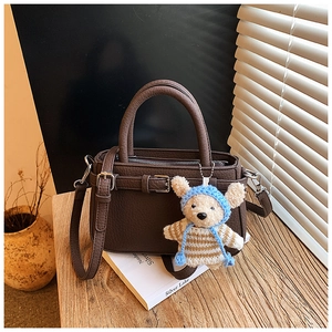 Detail of dark brown leather tote with fine texture, belt buckle, and cute bear charm