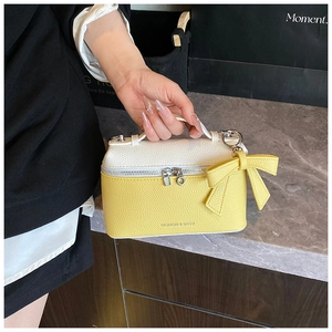 Detail of lychee pattern leather box bag with yellow bow and metal zippers