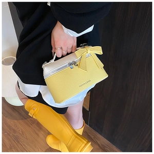 Detail of yellow lychee leather box bag with cream lid and decorative 3D bow accent